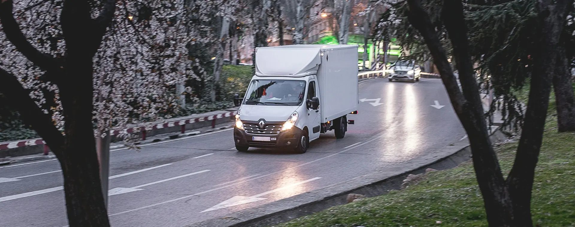 A delivery truck on a wet road at dusk with headlights on